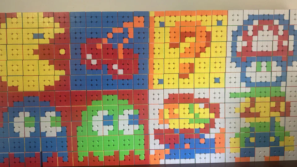A large mosaic made from Rubik's cubes arranged into retro pixel‑art: Pac‑Man, cherries, ghosts, Mario, Luigi, a question block, and a mushroom.